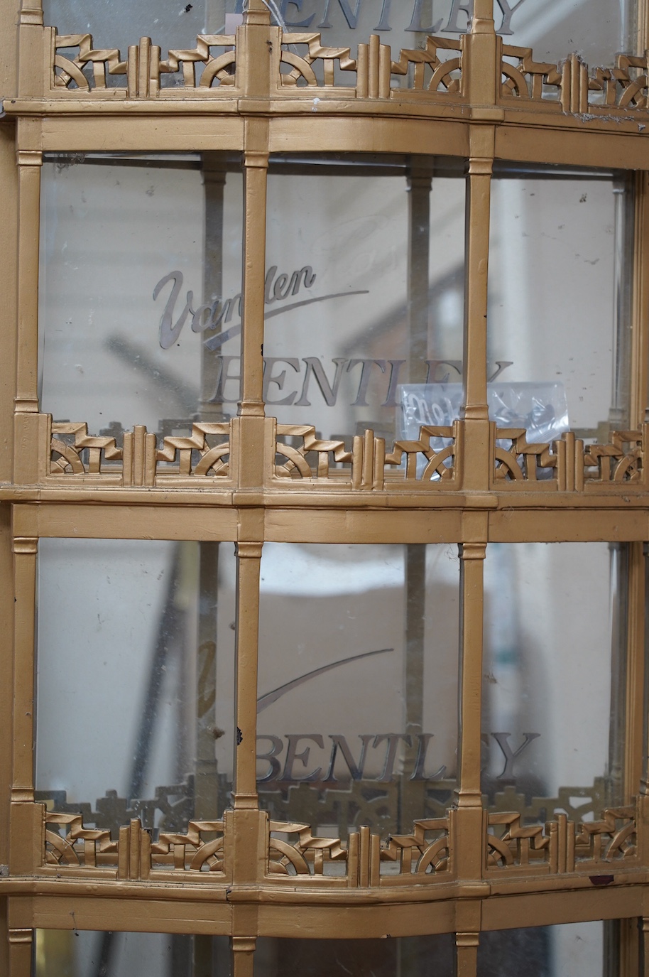 A 1920s gold-painted and mirror backed bow fronted Vanden Plas Bentley mirror-backed automobile showroom display unit, with five galleried shelves in an Art Deco style, each with bevelled mirrors behind and applied lette